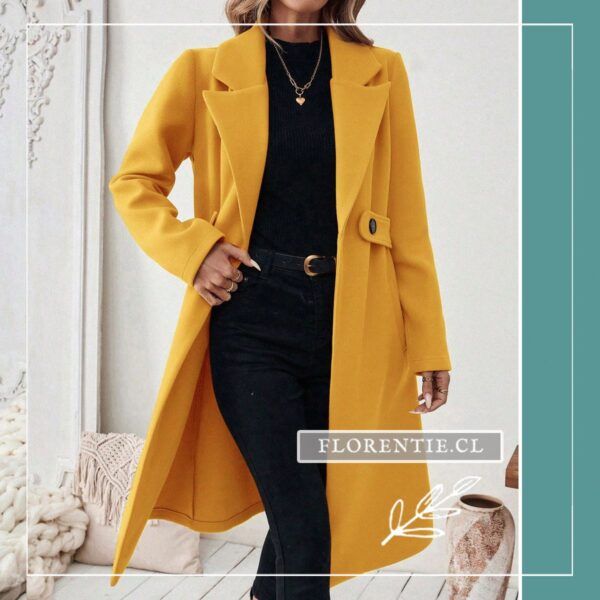 Modelo de frente con abrigo amarillo mujer de corte sastre, solapas amplias y outfit negro monocromático, mano en cadera