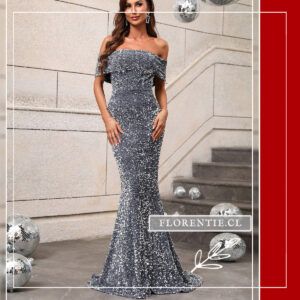 Vista frontal lateral del vestido de fiesta largo plateado oscuro con bordado completo de lentejuelas, escote bardot con doblez y silueta sirena de cola extendida, modelo con mano sobre el pecho en exterior con escalera y bolas disco.