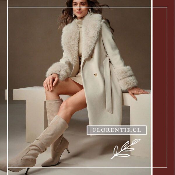Modelo sentada luciendo abrigo largo blanco crema con cuello y puños de pelo sintético, combinado con botas altas beige.