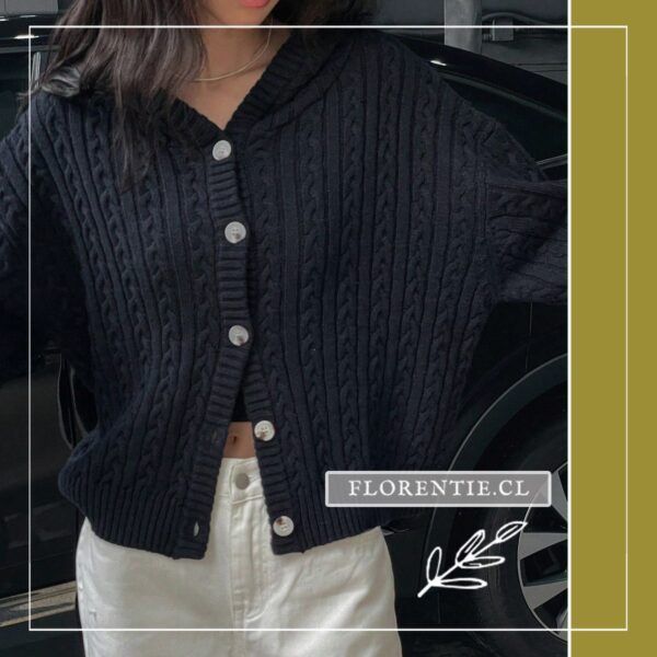 Vista frontal completa del cardigan azul marino con capucha y abotonadura nacarada, trenzas verticales en relieve, sobre jeans blancos y top negro.