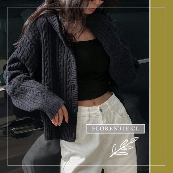 Modelo sosteniendo el cardigan azul marino abierto mostrando el escote en V natural y capucha, tejido cable knit oversize con pantalón blanco.