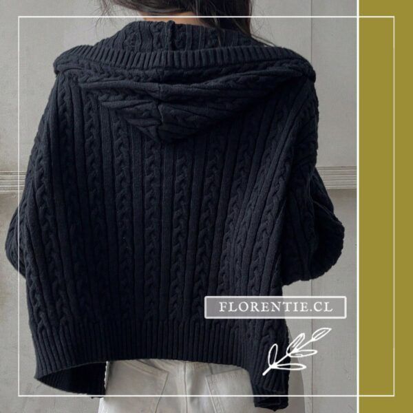 Vista posterior del cardigan azul marino cable knit mostrando la capucha integrada y el patrón de trenzas verticales en espalda completa, con pantalón blanco.
