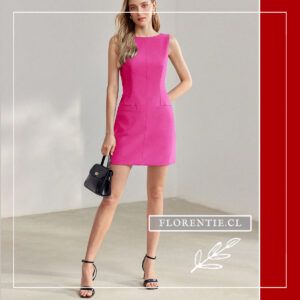 Modelo con vestido mini fucsia de corte recto entallado, escote bateau y bolsillos frontales decorativos, sujetando bolso negro de asa, fondo neutro grisáceo.