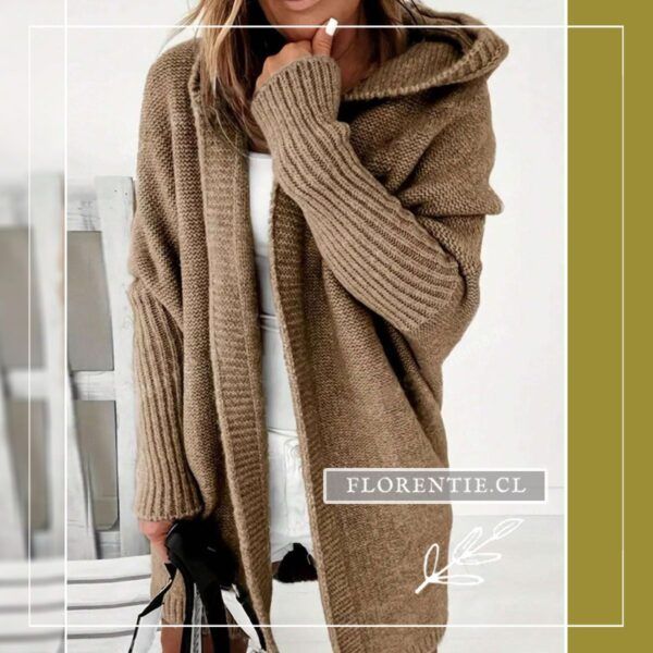 Modelo con cárdigan largo camel de capucha amplia sobre top blanco, manos cerca del rostro, tejido punto grueso con puños acanalados y cartera negra.