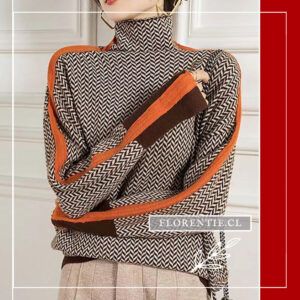 Vista frontal del sweater de cuello alto tortuga con patrón chevron bicolor en tonos tierra y acentos naranjas, look urbano con falda tableada beige.