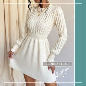 Modelo de frente con vestido blanco crema de tejido trenzado en cuerpo y mangas, cintura ceñida y falda evasé, collar dorado con dije, fondo neutro.