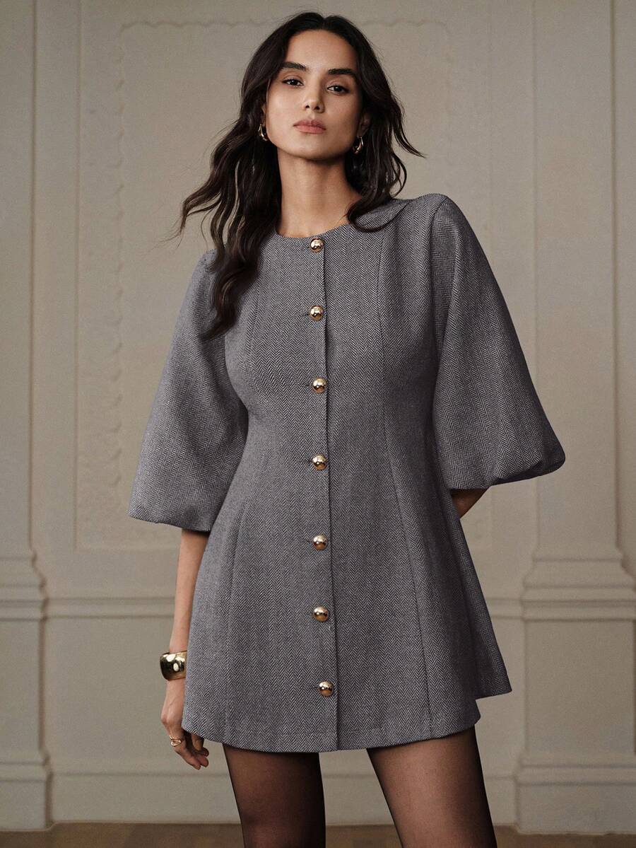 Look completo con vestido corto gris manga campana, medias semiopacas negras, brazalete dorado y aros en ambiente elegante interior