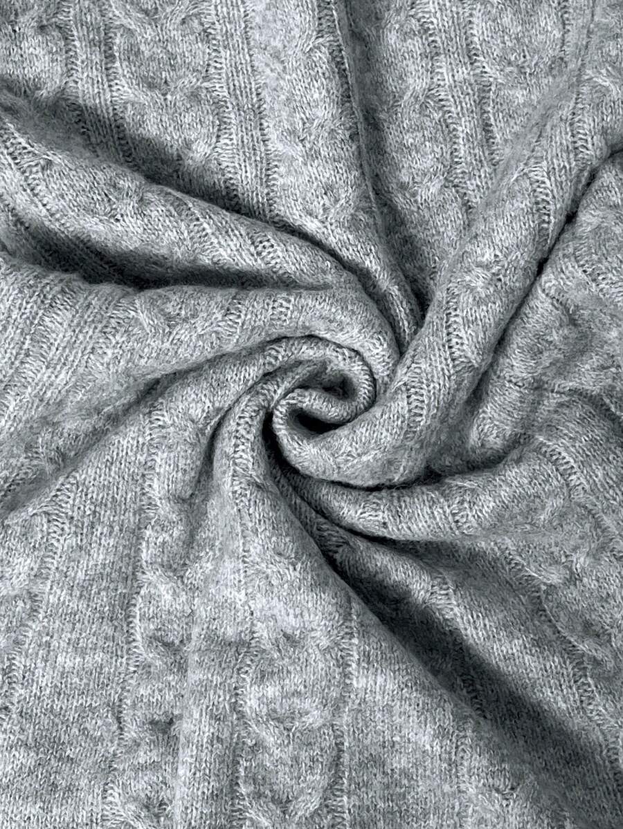 Primer plano del tejido de punto gris jaspeado con patrón de trenzas en espiral mostrando la textura suave y artesanal del material