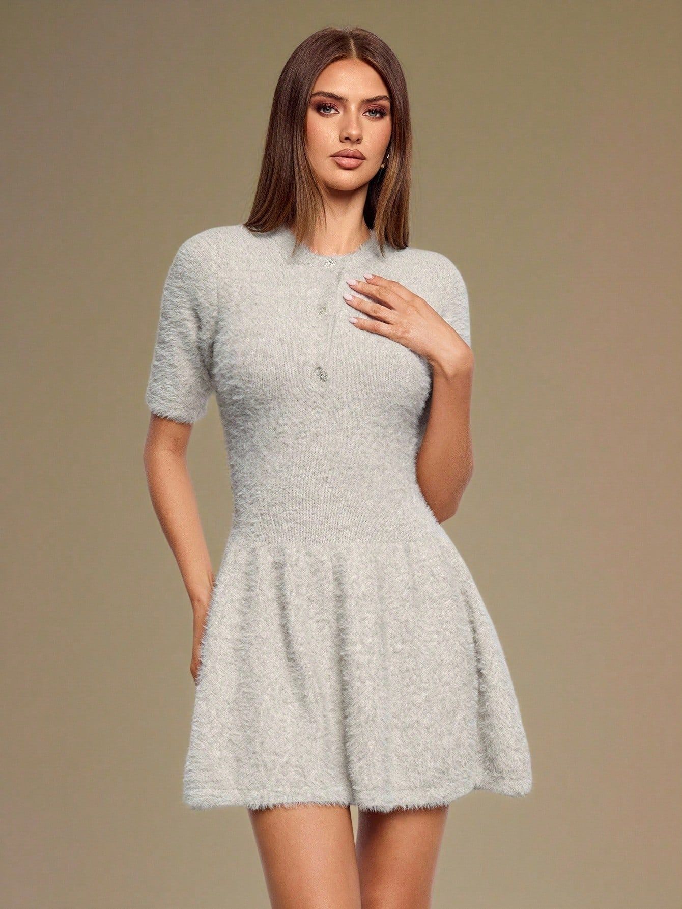 Modelo posando con vestido gris peludo entallado en cintura, mano en el pecho mostrando botones decorativos y falda con vuelo