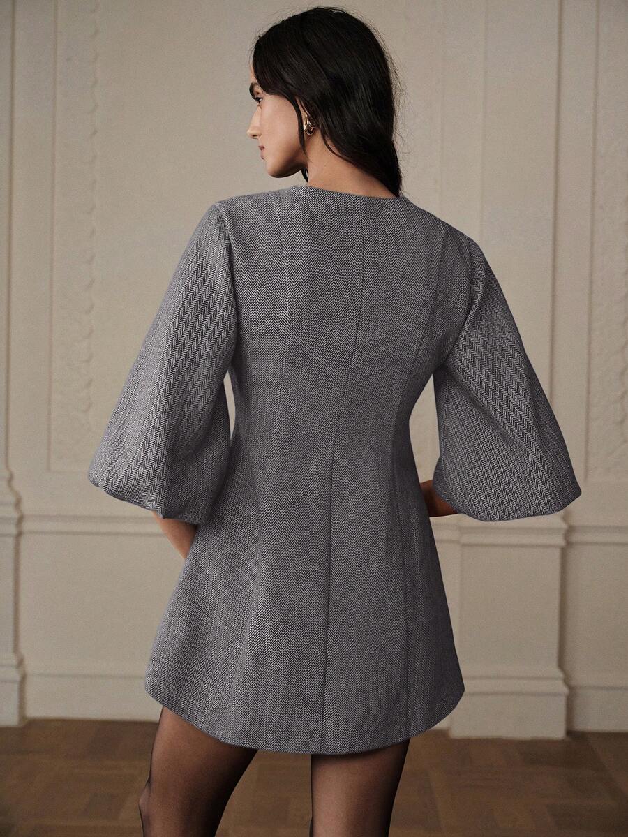 Vista posterior de vestido corto gris espiga mostrando espalda lisa, mangas campana y caída fluida sobre modelo con aros dorados