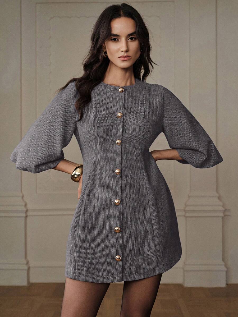 Modelo en pose con manos en cintura luciendo vestido corto gris con manga campana, brazalete dorado y botones esféricos