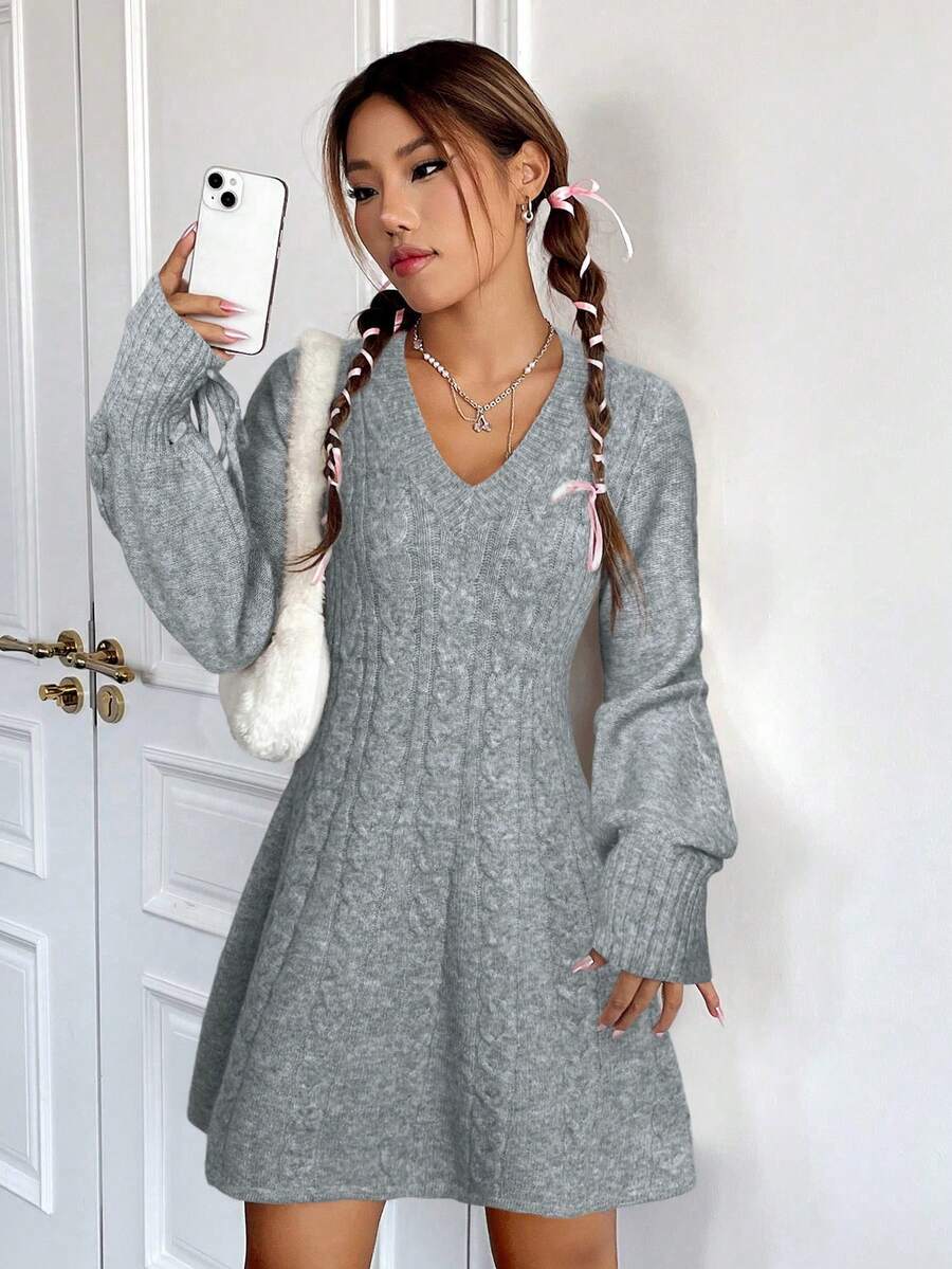 Mujer tomando selfie con vestido gris de punto trenzado, escote V, mangas abullonadas, collar delicado y bolso peluche blanco al hombro