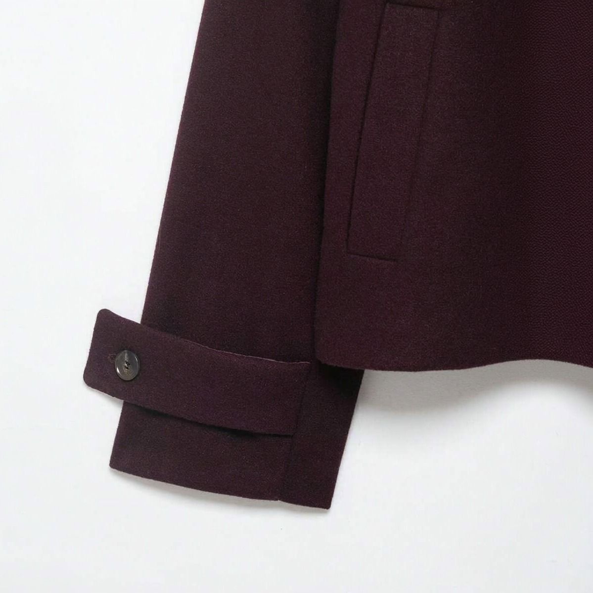 Detalle del puño con trabilla y botón del abrigo corto burgundy, bolsillo lateral de vivo visible