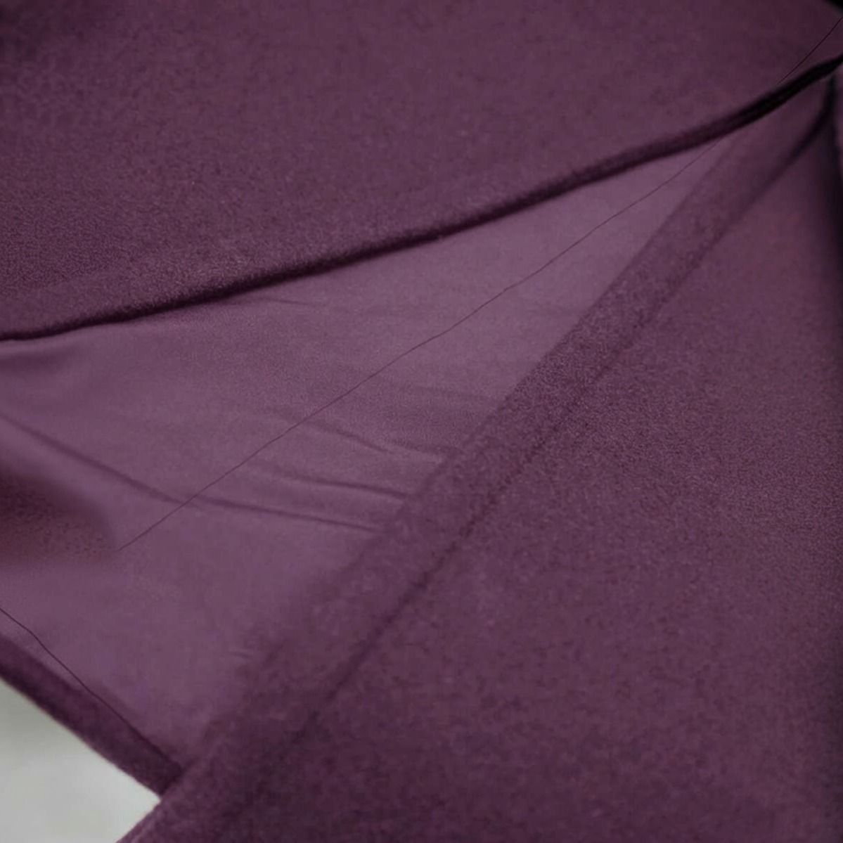 Detalle macro del tejido del abrigo morado mostrando textura de paño suave, costuras interiores y forro violeta