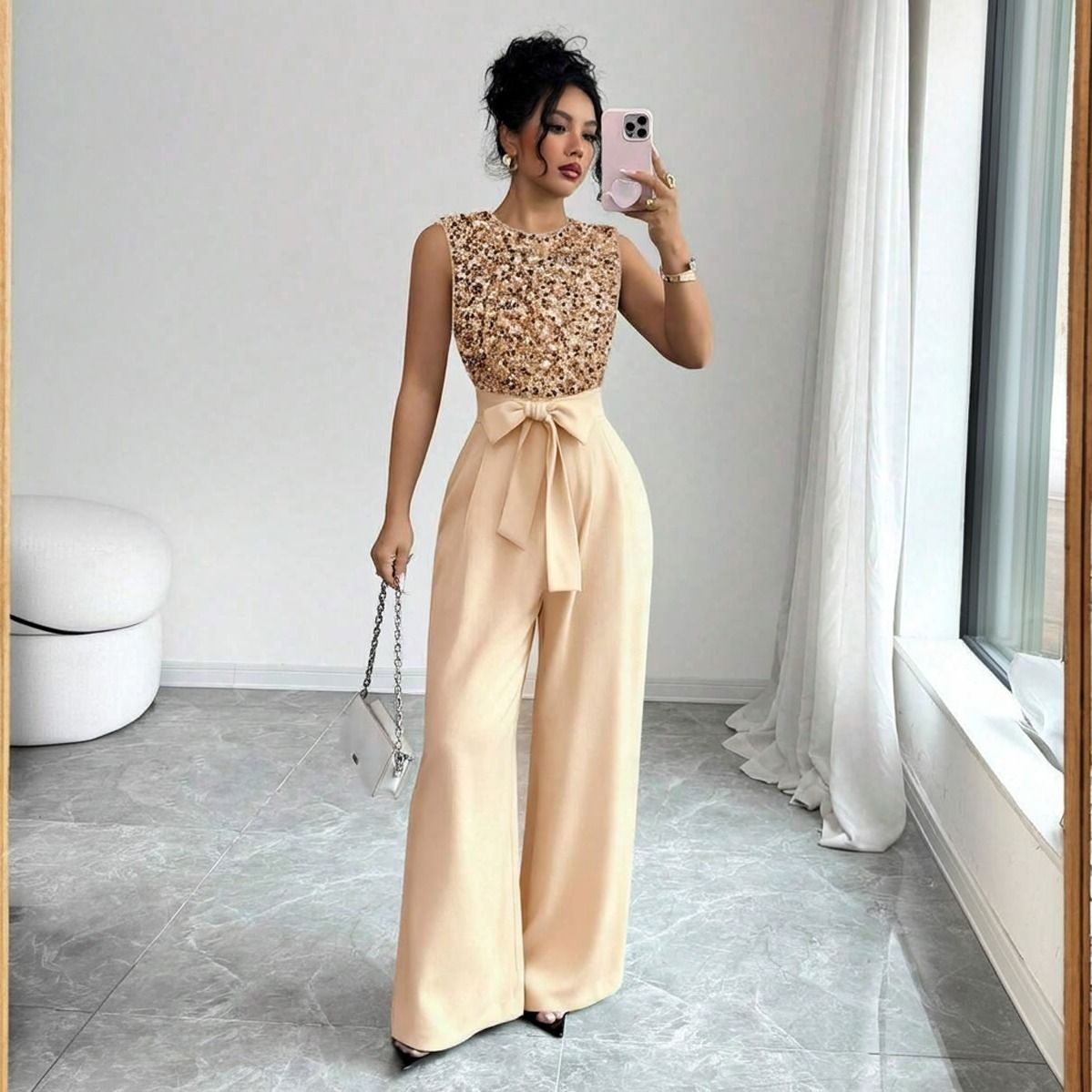 Mujer con enterito dorado de lentejuelas y lazo en cintura tomando selfie con clutch plateado de cadena