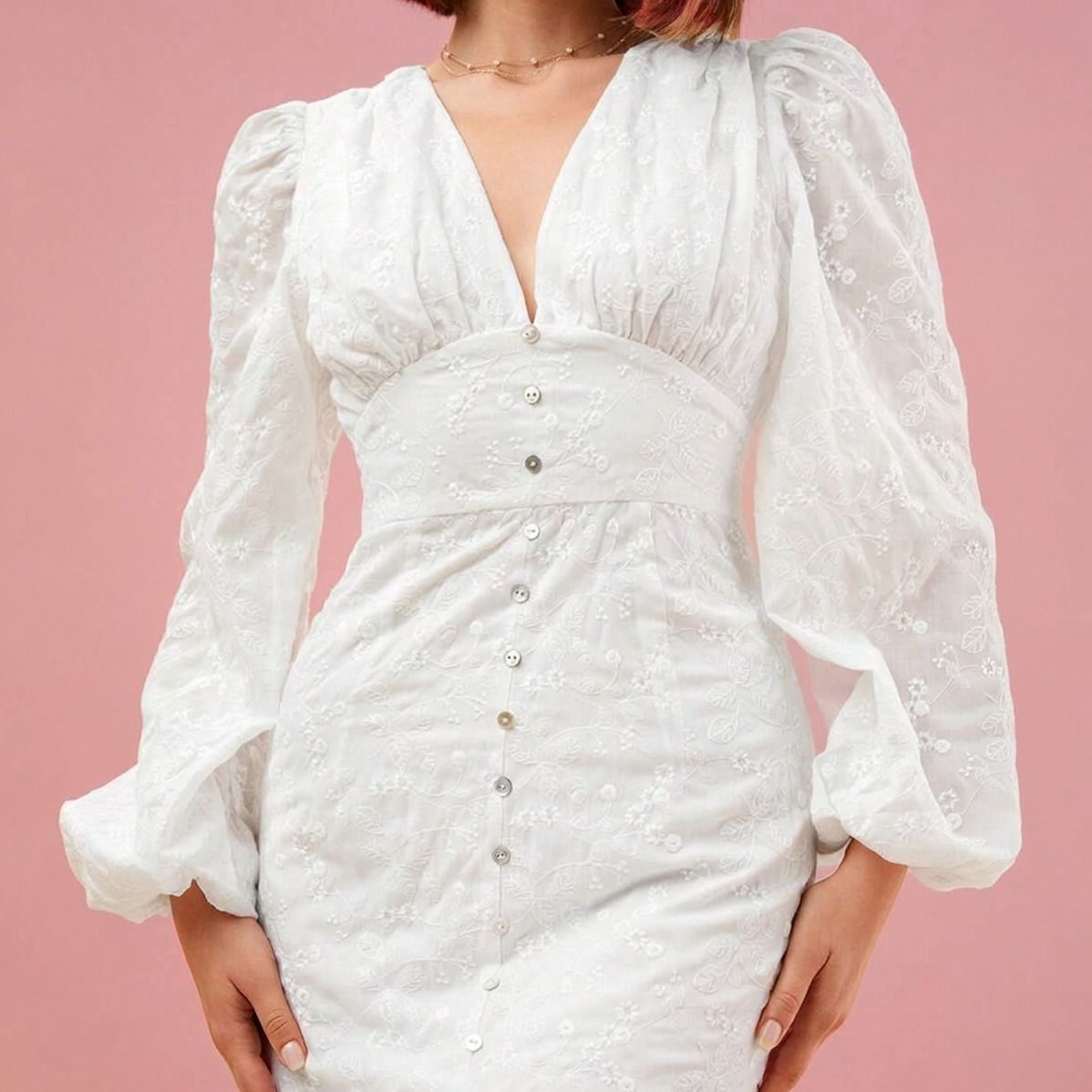 Detalle de bordado floral en relieve, escote V, botones pequeños y mangas globo con transparencia en vestido blanco