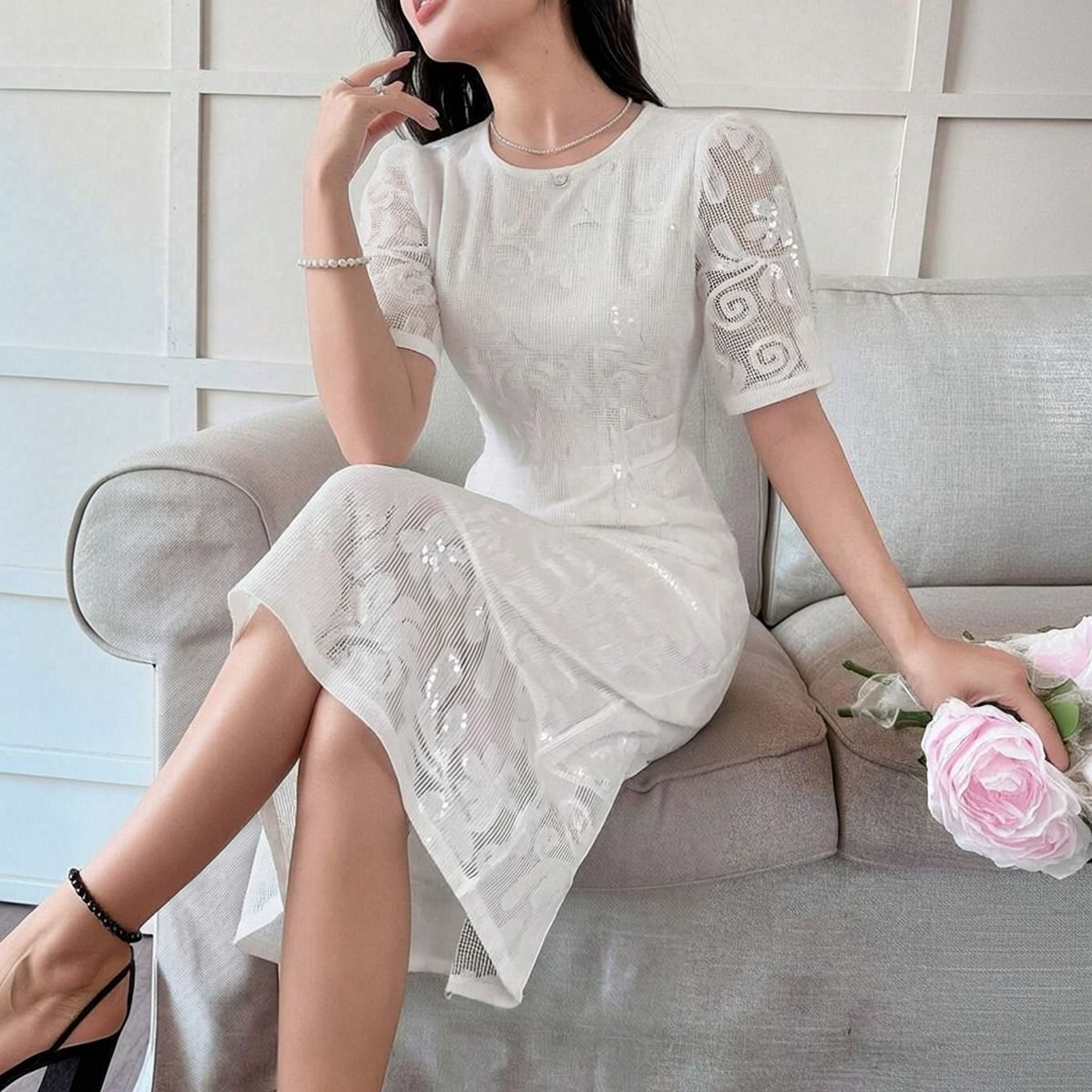 Modelo sentada en sofá con vestido blanco de encaje mostrando la caída de la falda midi y transparencia del ruedo