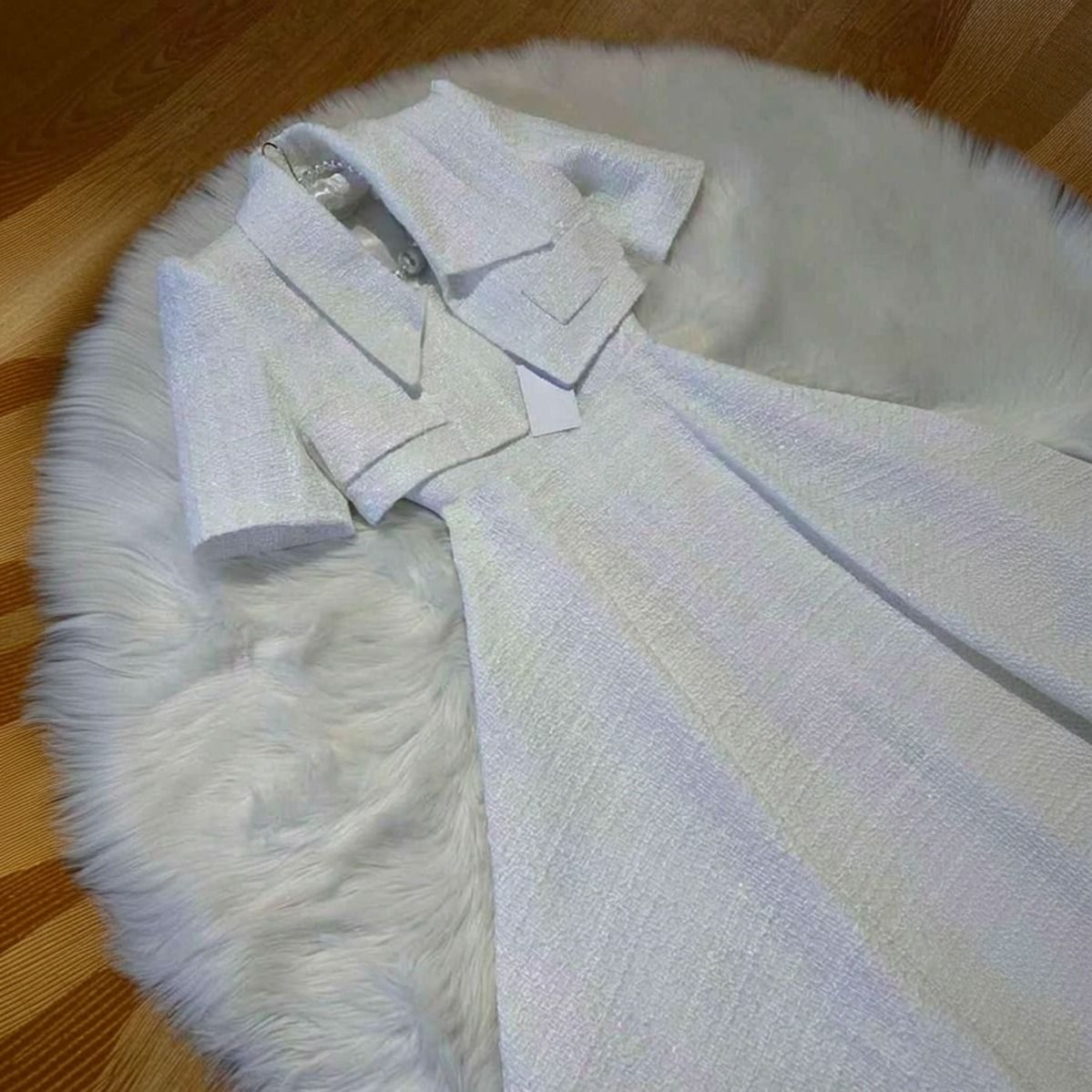 Flatlay del conjunto vestido y chaqueta cropped tweed blanco extendido sobre superficie, detalle de textura
