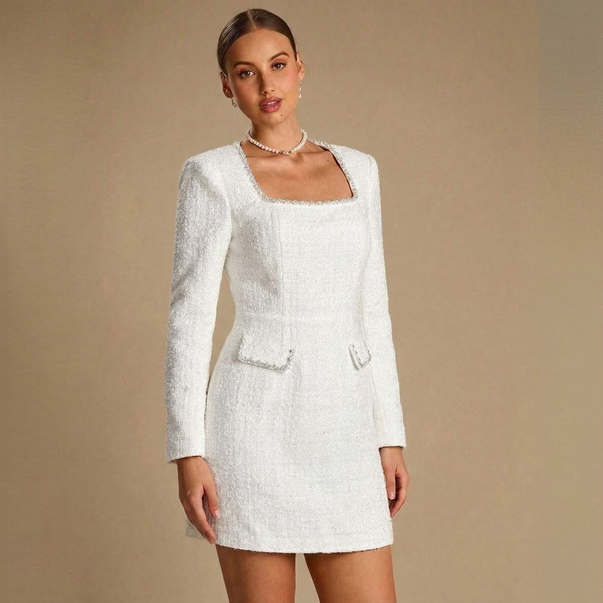 Plano medio frontal de vestido corto de tweed blanco con manga larga y escote cuadrado sobre fondo beige
