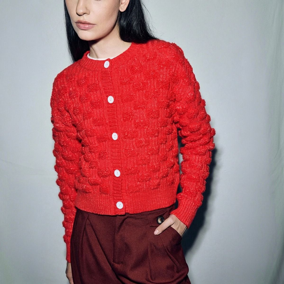 Cardigan rojo de punto con textura floral en relieve y botones blancos visto de frente en plano medio
