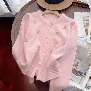 Cardigan rosa pastel con botones de perla y aplicaciones de cerezas bordadas visto de frente sobre mesa