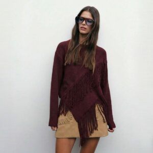 Sweater tejido burdeo con flecos diagonales y manga larga visto de frente sobre minifalda camel