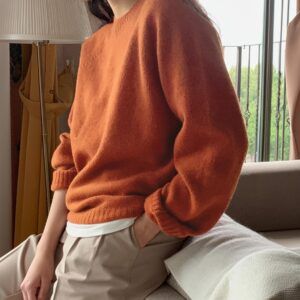 Sweater coral oversize de punto con cuello redondo y mangas globo, vista lateral sobre sofá