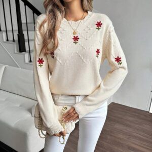 Sweater tejido crema con flores rojas bordadas y textura de rombos visto de frente sobre modelo con jeans blancos