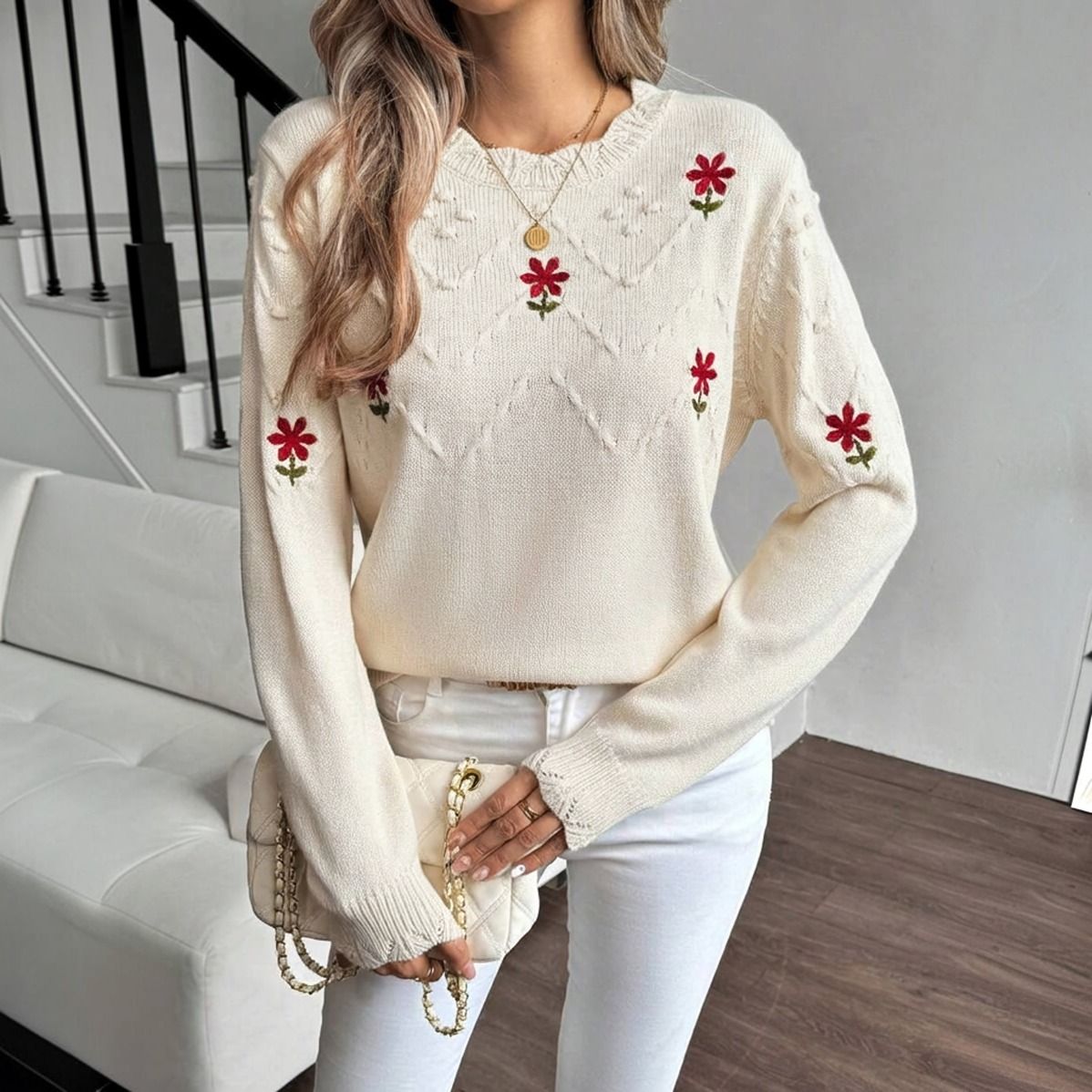 Sweater tejido crema con flores rojas bordadas y textura de rombos visto de frente sobre modelo con jeans blancos