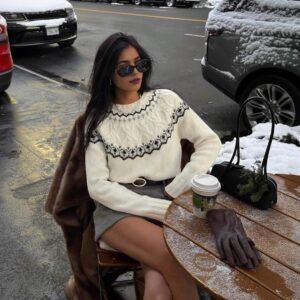 Mujer sentada en terraza con sweater crema de jacquard nordico negro combinado con minifalda gris