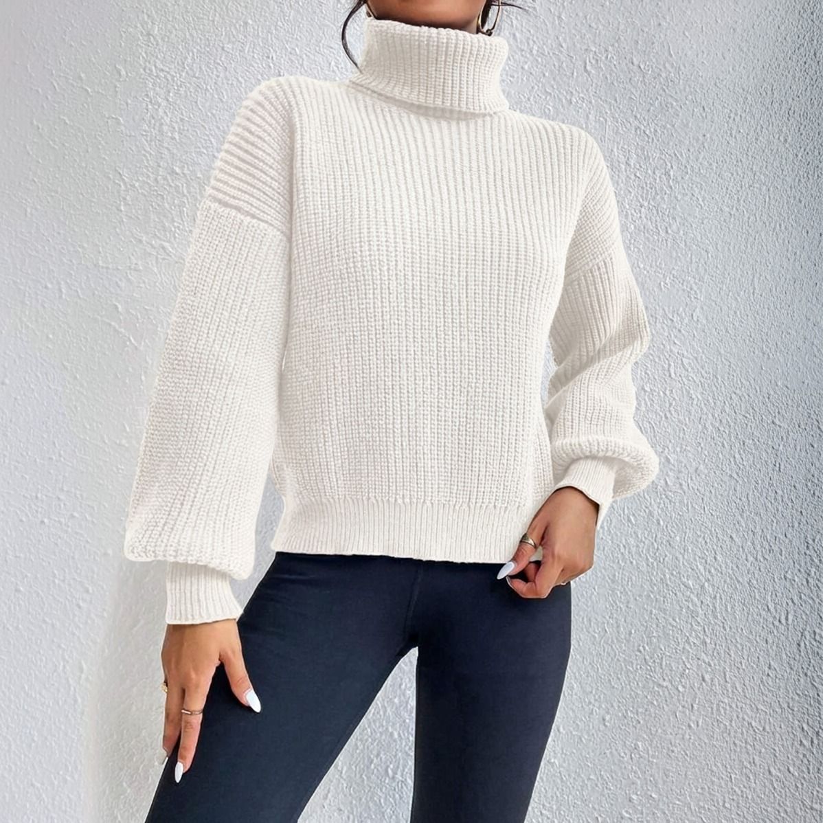 Vista lateral de sweater cuello tortuga crudo mostrando caida de manga murcielago y largo cropped sobre calzas negras