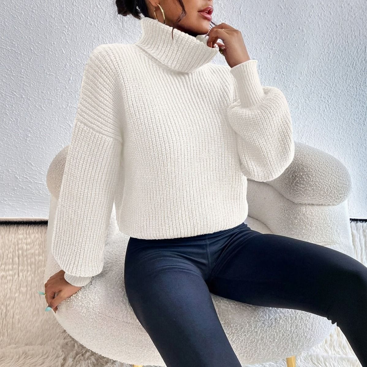 Mujer sentada con sweater cuello tortuga crudo de punto acanalado y mangas murcielago sobre calzas negras