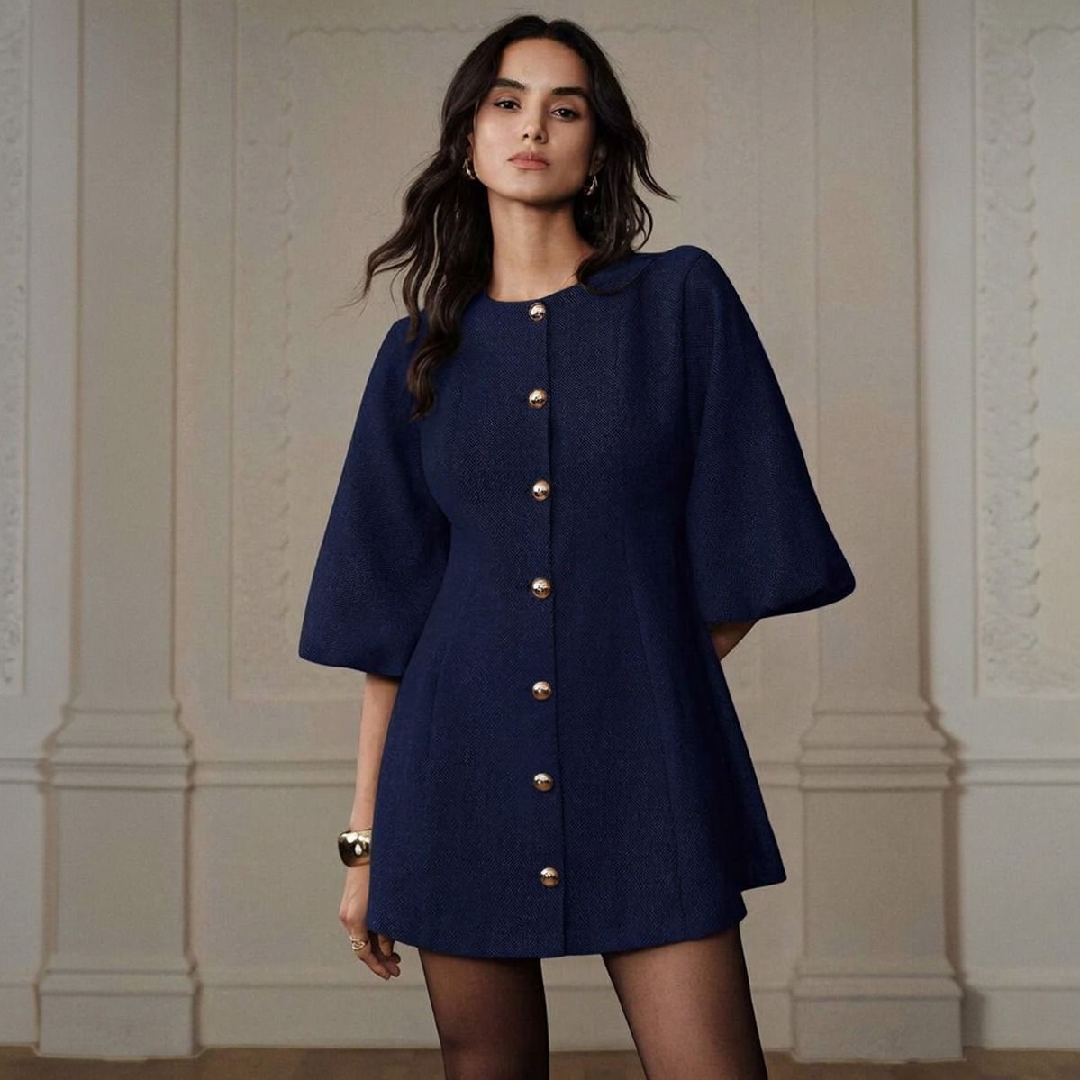Vestido corto azul marino con siete botones dorados esféricos y mangas abullonadas tres cuartos, pose frontal con brazaletes dorados