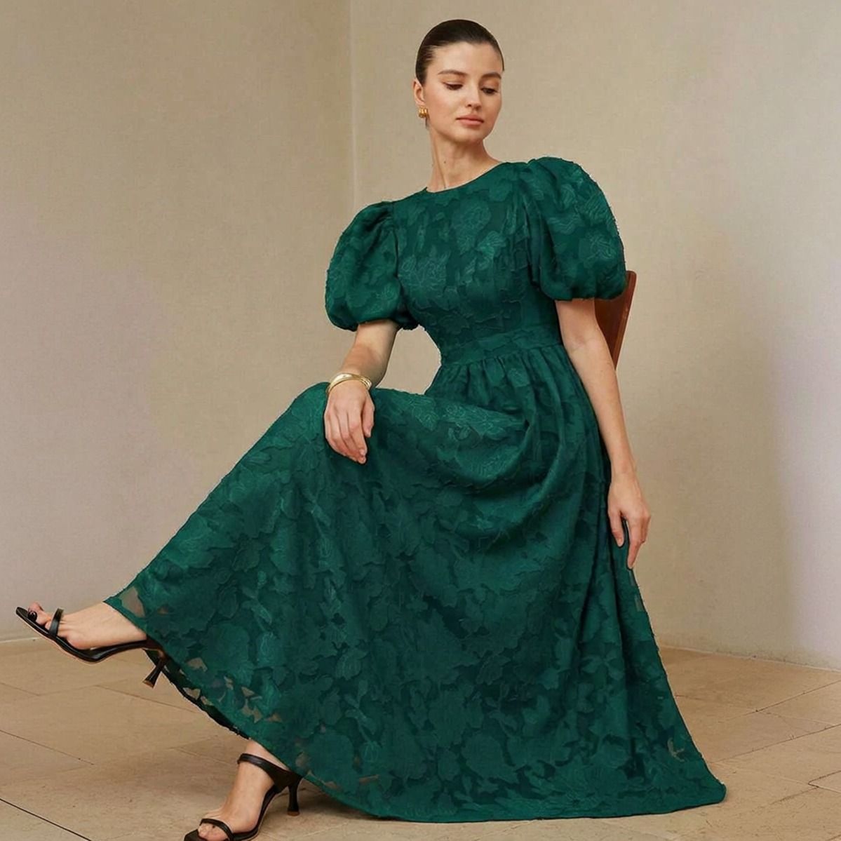 Modelo sentada con vestido verde esmeralda largo midi en jacquard floral con mangas abullonadas cortas y escote redondo