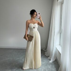 Mujer con enterito marfil strapless de pierna ancha plisada, tomada de perfil frente a un espejo con clutch café