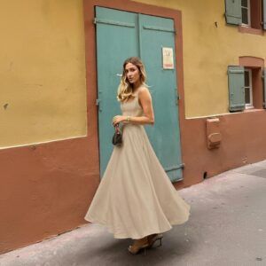 Mujer caminando con vestido maxi beige evasé con tirantes anchos y escote cuadrado vista lateral en calle
