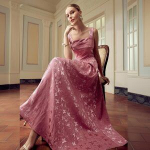 Mujer sentada con vestido maxi rosa antiguo en jacquard floral con tirantes anchos y falda evasé amplia