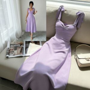 Vestido midi lila con tirantes de lazo y escote corazón extendido sobre sofá beige junto a bolso crema