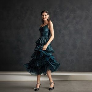 Vestido midi verde petróleo con cuerpo drapeado y falda de volantes plisados en cascada, vista frontal en movimiento