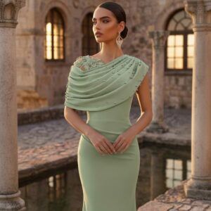 Vestido verde salvia visto de medio cuerpo con capa drapeada de perlas y encaje floral en el hombro izquierdo